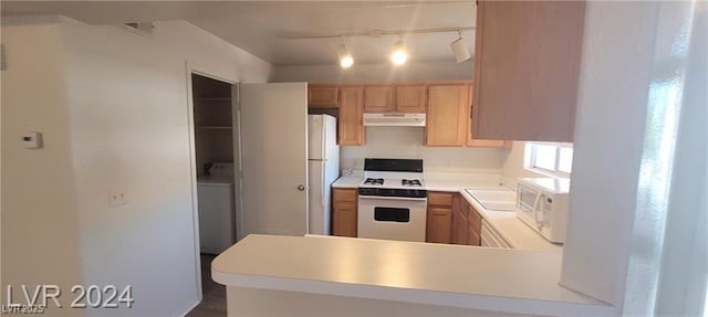 kitchen with white appliances, washer / dryer, light countertops, under cabinet range hood, and a sink