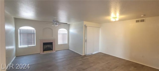 unfurnished living room featuring a fireplace with raised hearth, wood finished floors, visible vents, and a ceiling fan