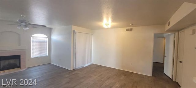 unfurnished living room with a ceiling fan, visible vents, a tiled fireplace, and wood finished floors