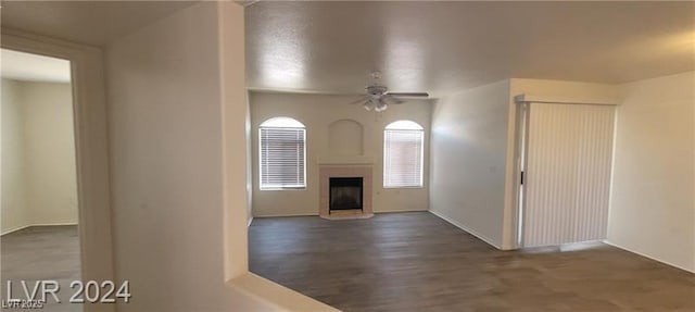 unfurnished living room with ceiling fan, a fireplace with raised hearth, and wood finished floors