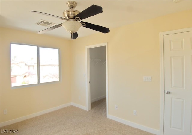 unfurnished bedroom featuring light colored carpet, visible vents, a spacious closet, and baseboards