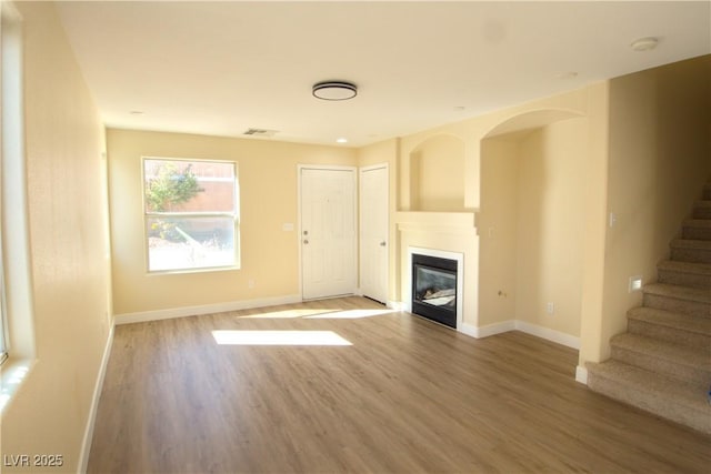 unfurnished living room with a glass covered fireplace, wood finished floors, baseboards, and stairs