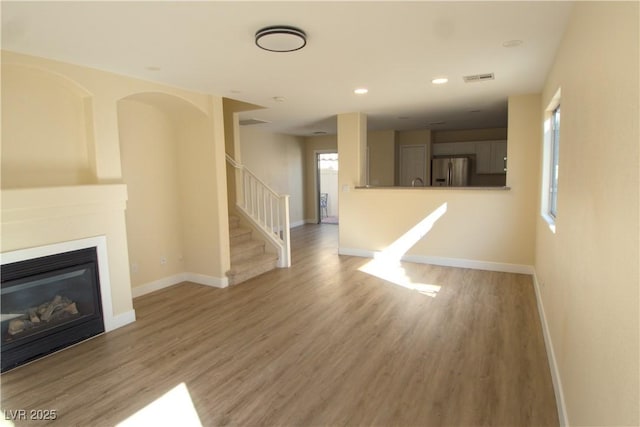 unfurnished living room with visible vents, baseboards, a glass covered fireplace, wood finished floors, and stairs