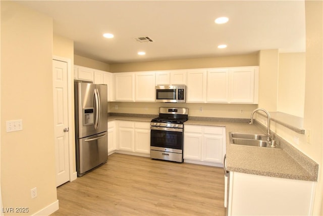 kitchen featuring light wood-style flooring, appliances with stainless steel finishes, white cabinetry, a sink, and recessed lighting