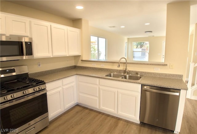 kitchen with light wood-type flooring, white cabinetry, appliances with stainless steel finishes, and a sink