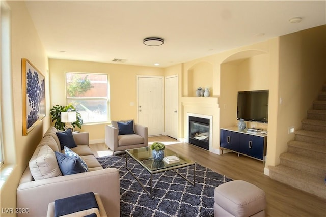 living room with visible vents, a glass covered fireplace, wood finished floors, baseboards, and stairs