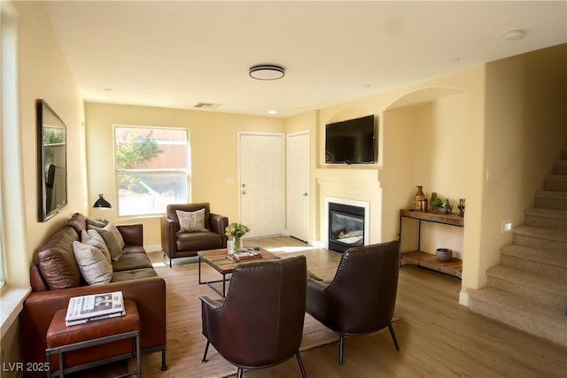 living area with stairs, visible vents, wood finished floors, and a glass covered fireplace