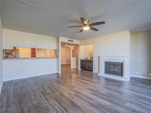 unfurnished living room featuring a brick fireplace, wood finished floors, visible vents, and a ceiling fan