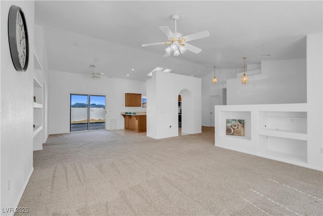 unfurnished living room featuring arched walkways, lofted ceiling, light carpet, a ceiling fan, and built in features