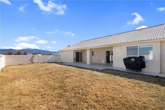 rear view of house with a fenced backyard, a tile roof, a yard, a patio area, and stucco siding