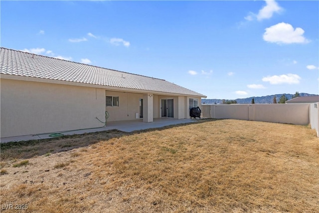 rear view of house featuring a yard, a patio, stucco siding, a fenced backyard, and a tiled roof