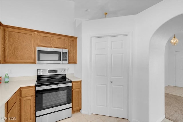 kitchen featuring arched walkways, light countertops, appliances with stainless steel finishes, and brown cabinets