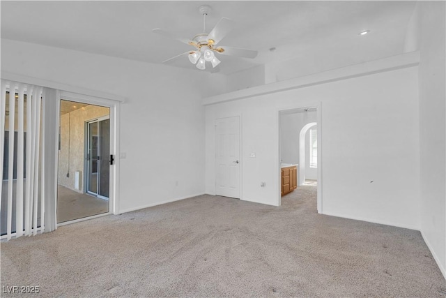 carpeted spare room with arched walkways and a ceiling fan