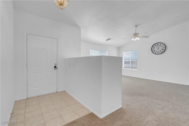 empty room with light tile patterned floors, visible vents, light colored carpet, lofted ceiling, and ceiling fan