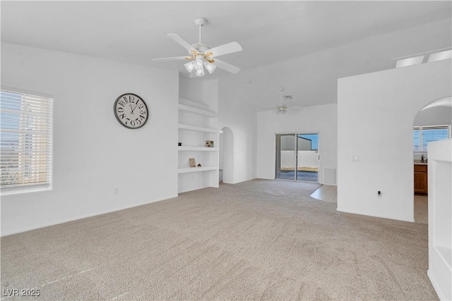 unfurnished living room featuring carpet floors, arched walkways, built in shelves, vaulted ceiling, and ceiling fan