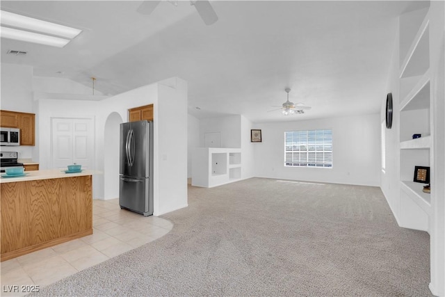 unfurnished living room with visible vents, arched walkways, a ceiling fan, light colored carpet, and built in shelves