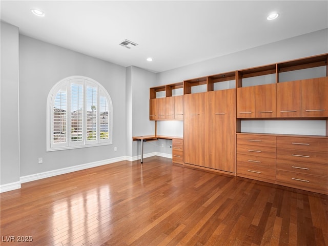 unfurnished living room featuring baseboards, visible vents, dark wood finished floors, and built in study area