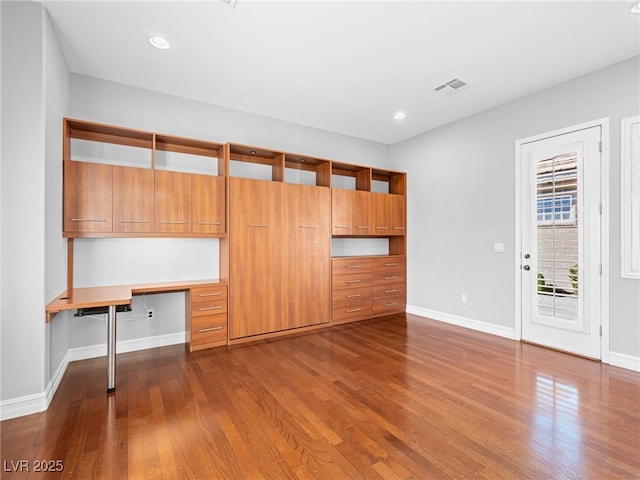 interior space with dark wood-type flooring, visible vents, built in desk, and baseboards