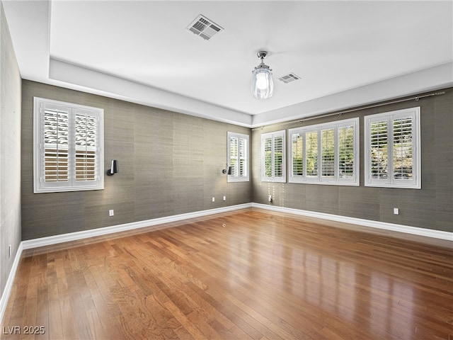 unfurnished room with hardwood / wood-style flooring, visible vents, and baseboards