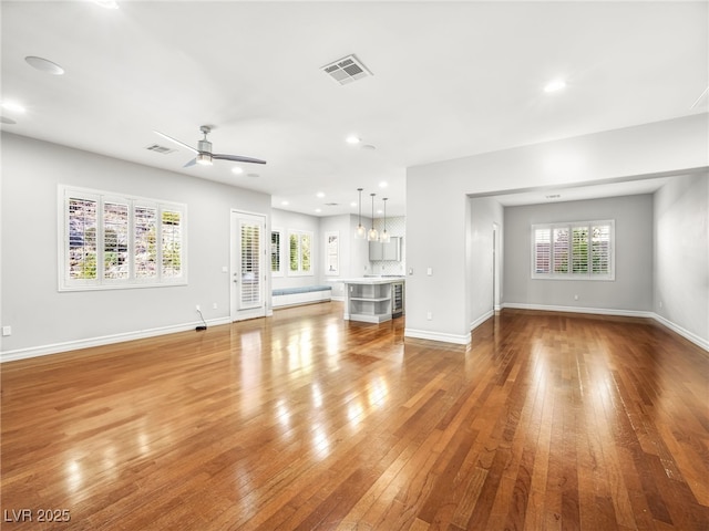 unfurnished living room featuring a ceiling fan, baseboards, visible vents, and hardwood / wood-style floors