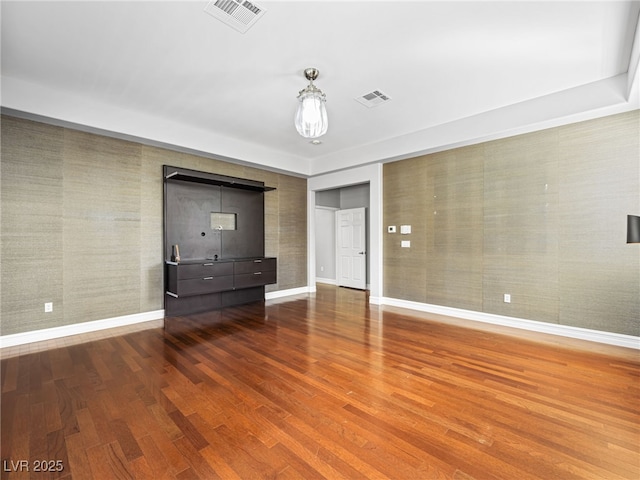 empty room featuring wood finished floors, visible vents, and baseboards