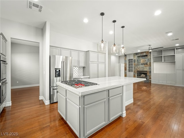 kitchen featuring a fireplace, visible vents, appliances with stainless steel finishes, a center island, and dark wood-style floors