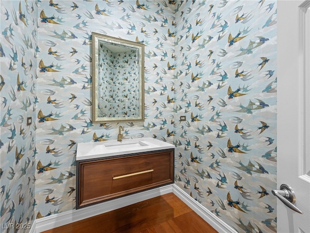 bathroom featuring baseboards, wood finished floors, vanity, and wallpapered walls