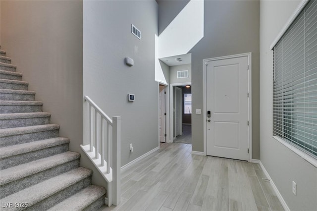 foyer entrance featuring light wood-style floors, a high ceiling, visible vents, and stairs