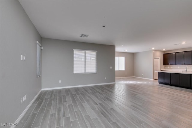 unfurnished living room with visible vents, baseboards, a sink, light wood-style floors, and recessed lighting