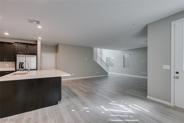 kitchen with stainless steel fridge with ice dispenser, visible vents, a sink, light countertops, and light wood-style flooring