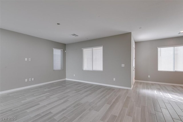 spare room with light wood-type flooring, a healthy amount of sunlight, baseboards, and visible vents