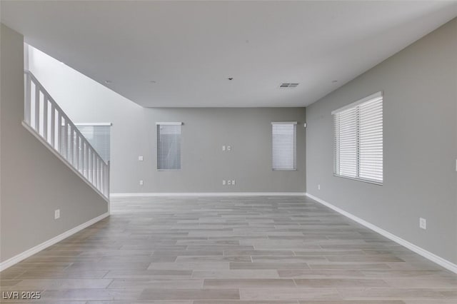 unfurnished living room with visible vents, baseboards, light wood finished floors, and stairway