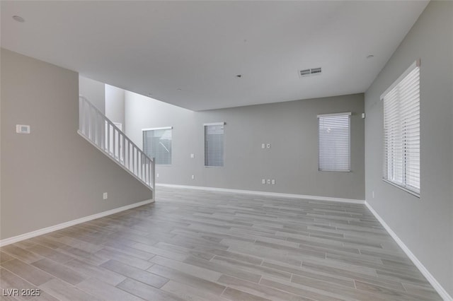 unfurnished living room with stairway, visible vents, light wood-type flooring, and baseboards
