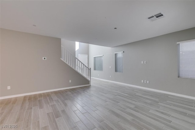 unfurnished living room with visible vents, baseboards, light wood finished floors, and stairway