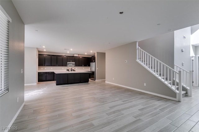 kitchen featuring baseboards, light wood-type flooring, open floor plan, light countertops, and stainless steel appliances