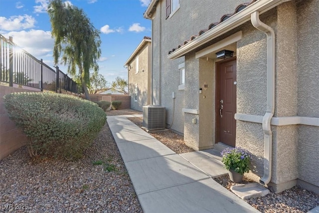 view of side of property with central AC, fence, and stucco siding