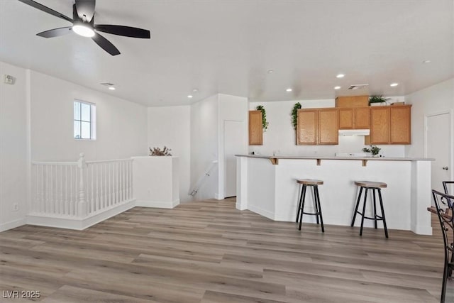 kitchen featuring a breakfast bar area, recessed lighting, under cabinet range hood, light countertops, and light wood finished floors