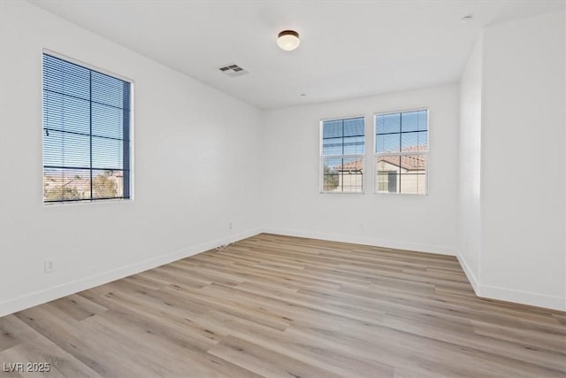 spare room featuring light wood finished floors, visible vents, and baseboards