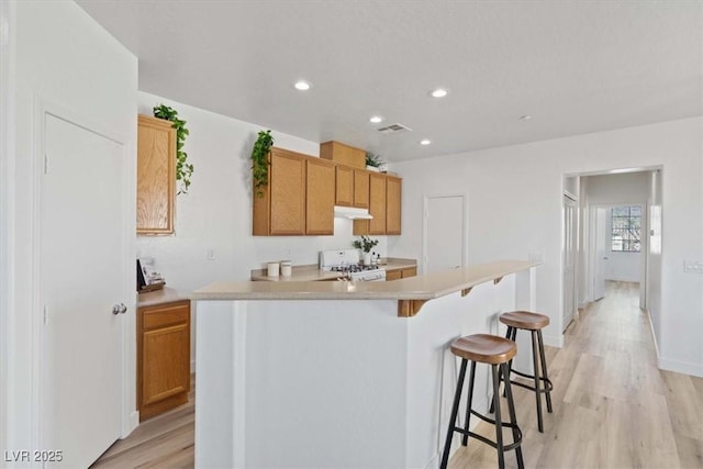 kitchen featuring white gas stove, under cabinet range hood, a breakfast bar, visible vents, and light countertops