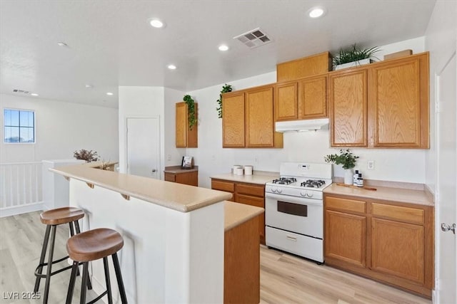 kitchen with a breakfast bar area, visible vents, a kitchen island, white range with gas stovetop, and under cabinet range hood