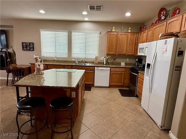 kitchen featuring light tile patterned flooring, white appliances, a breakfast bar, a kitchen island, and visible vents