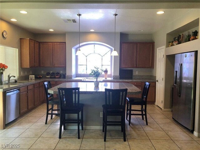 kitchen featuring visible vents, a sink, a kitchen breakfast bar, appliances with stainless steel finishes, and light tile patterned floors