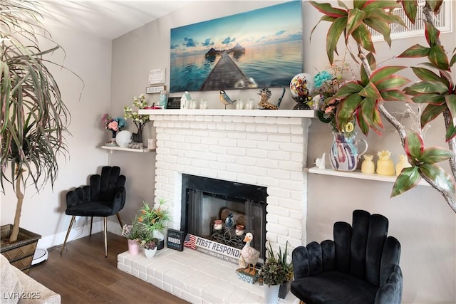 sitting room featuring a brick fireplace, baseboards, and wood finished floors