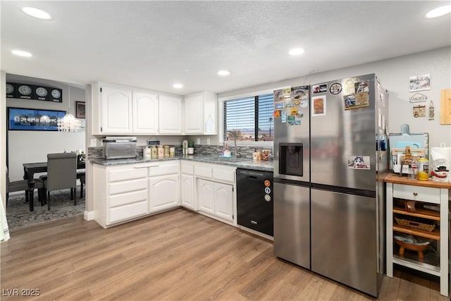 kitchen featuring light wood-style flooring, a sink, white cabinets, black dishwasher, and stainless steel fridge