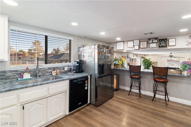 kitchen featuring stainless steel fridge, white cabinets, dishwasher, light wood-style floors, and a sink