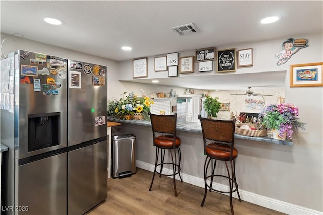 kitchen featuring recessed lighting, wood finished floors, visible vents, a kitchen breakfast bar, and stainless steel fridge