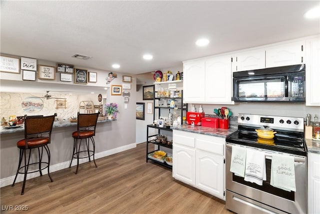 kitchen featuring a breakfast bar area, light wood finished floors, stainless steel electric stove, white cabinetry, and black microwave