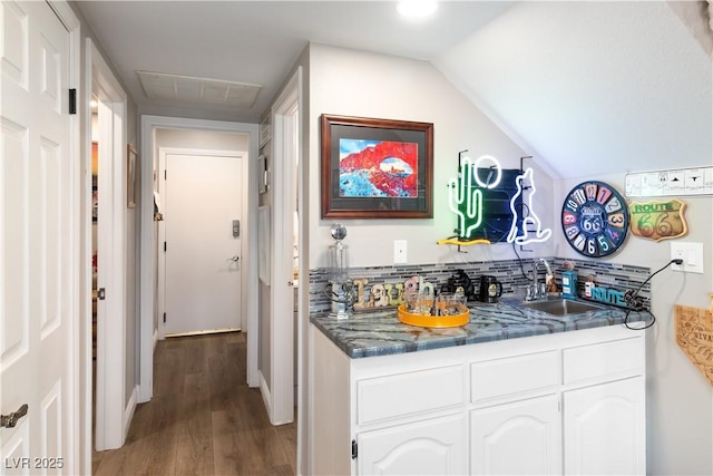 kitchen featuring visible vents, white cabinets, vaulted ceiling, a sink, and wood finished floors