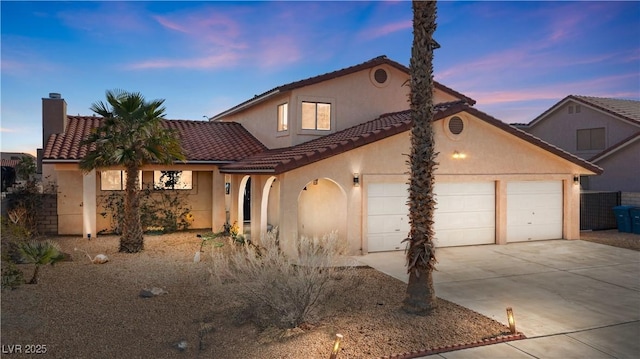 mediterranean / spanish house with driveway, a chimney, a tiled roof, an attached garage, and stucco siding