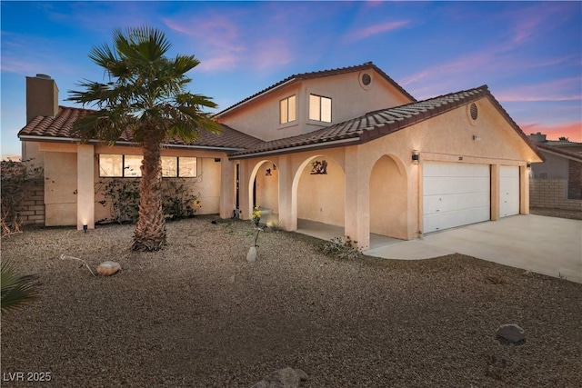 mediterranean / spanish home featuring a garage, concrete driveway, a tile roof, and stucco siding